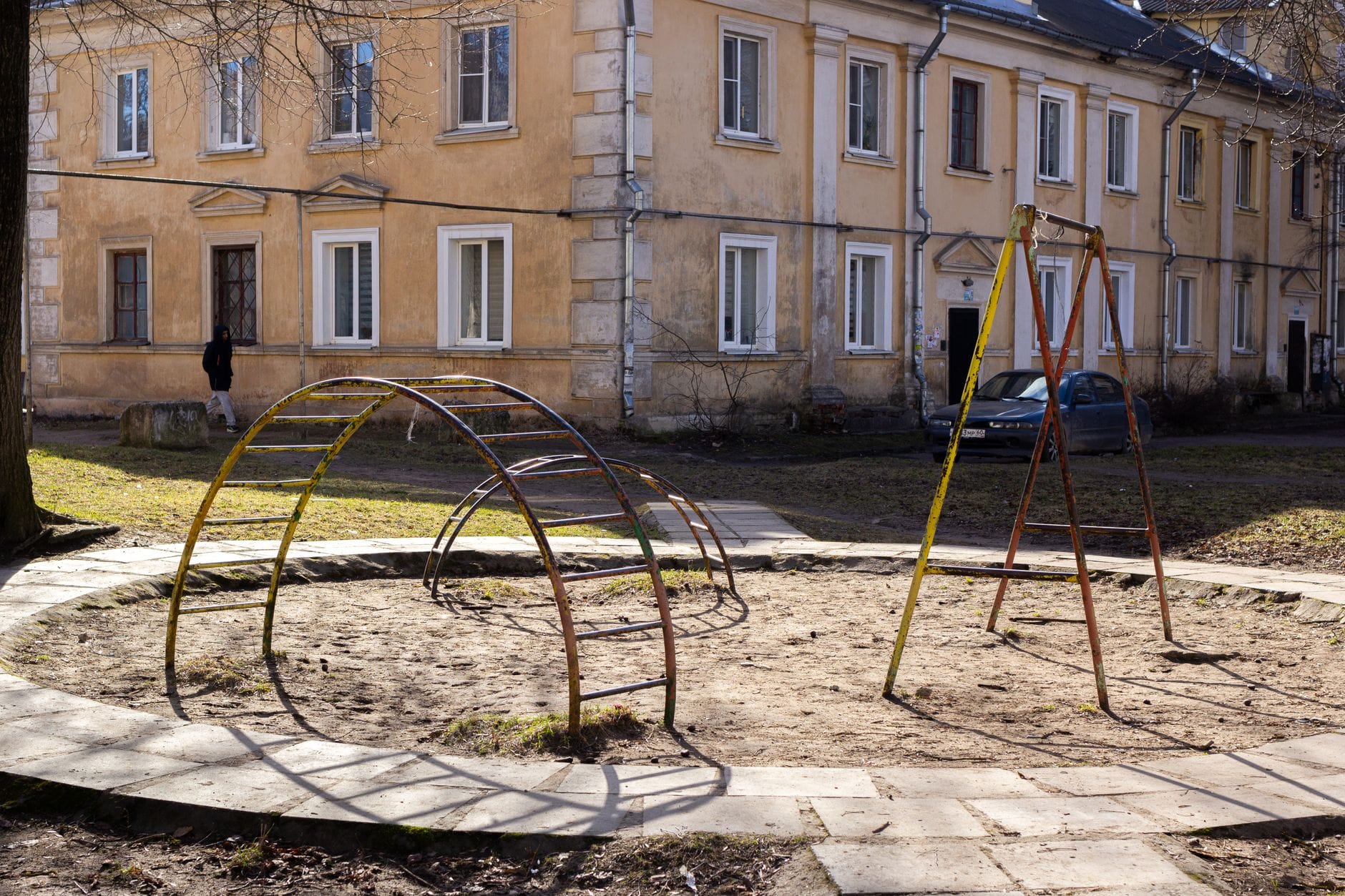 Stary plac zabaw z metalowymi drabinkami przy zniszczonym bloku